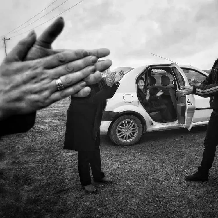 Preghiera e saluto tra persone vicino a auto, foto in bianco e nero; spiritualità e amicizia.