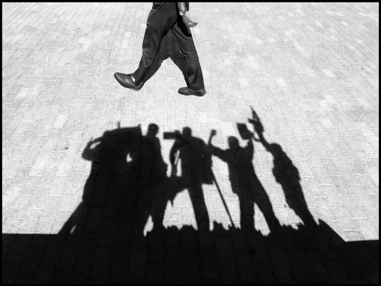Shadow di persone con accessori su strada, simbolo di street photography e arte visiva.