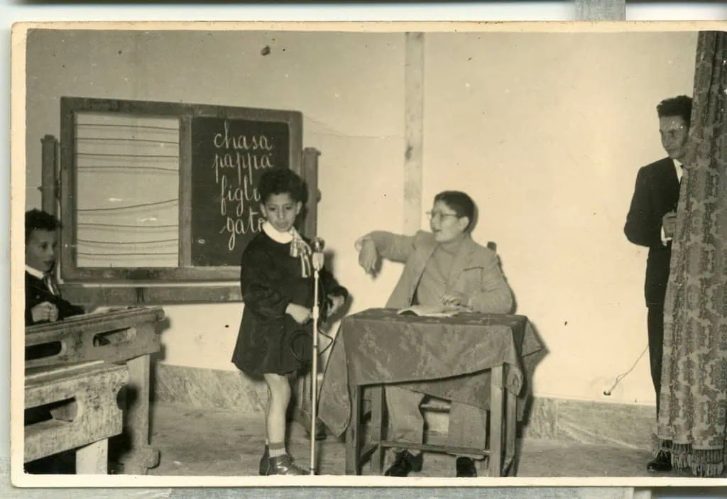 1. Bambina che parla in classe con insegnante e compagni in scuola vintage su Photoworld.