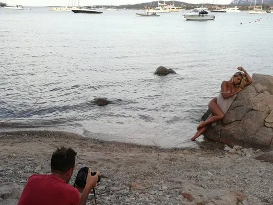 Scatto di una modella sulla spiaggia con yacht sullo sfondo, servizio fotografico marittimo all'aperto.