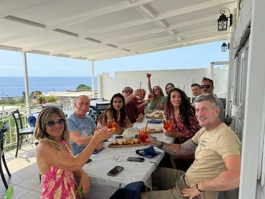 Persone che brindano a un pranzo all'aperto con vista mare, festa tra amici e familia, atmosfera estiva e conviviale.
