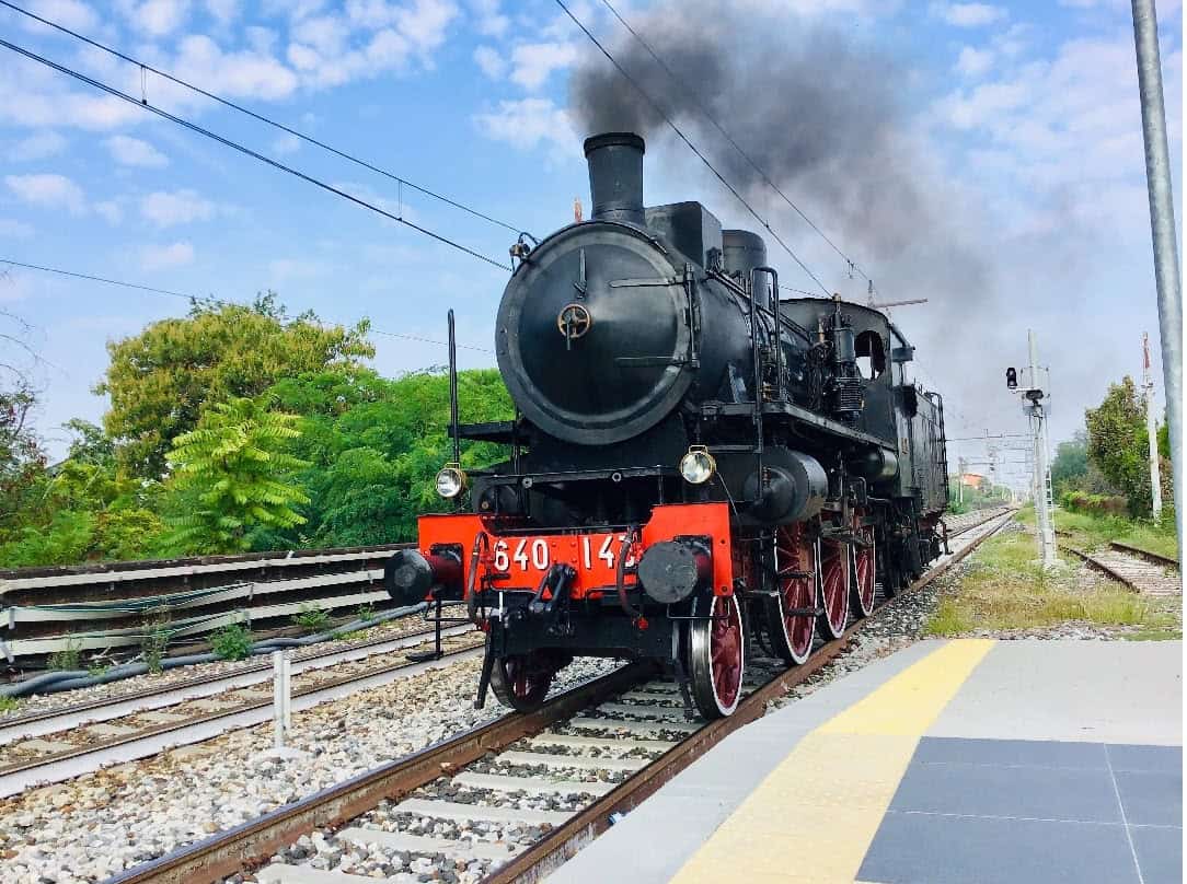 Vecchio treno a vapore nero su binari con sfondo naturale e cielo sereno.