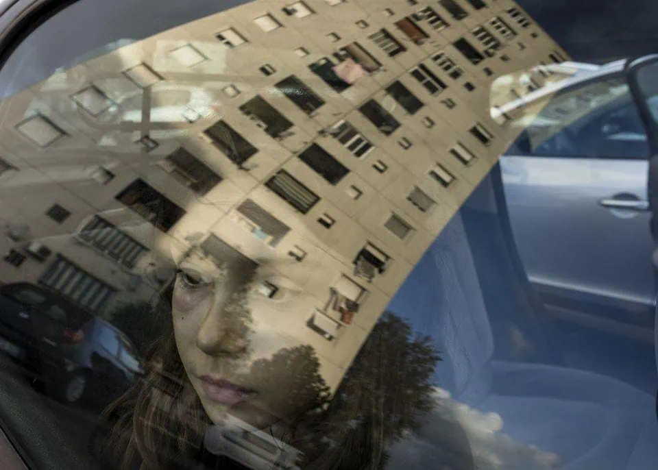 Riflesso di un palazzo su un'auto con una ragazza alla guida. Atmosfera urbana e riflessi suggestivi, esempio di fotografia contemporanea.