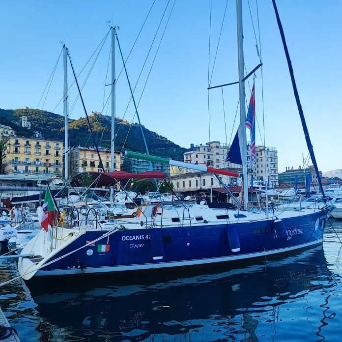 Barca a vela nel porto di Amalfi con edifici storici sullo sfondo.