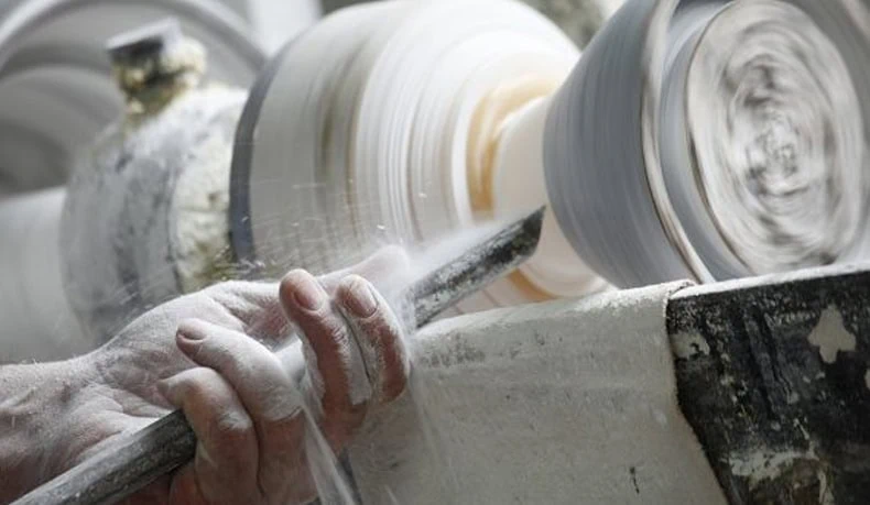Dettaglio di una mano che dipinge ceramiche con strumenti tradizionali.