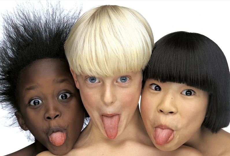 Foto di tre bambini con lingua fuori, espressioni giocose e spontanee.