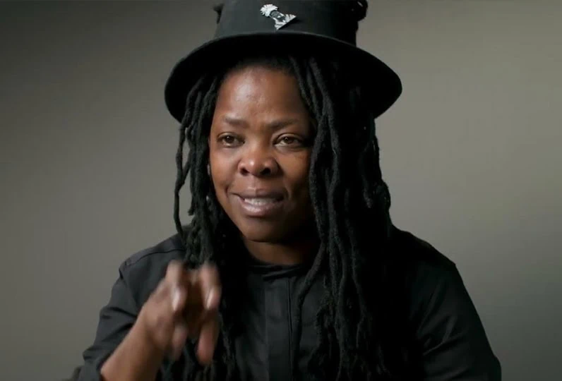 Donna con dreadlocks e cappello nero, espressione intensa.