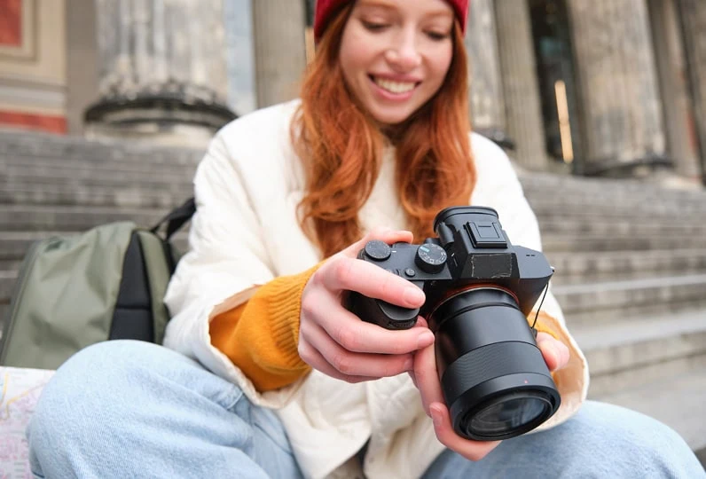 Donna con reflex digitale sorridente, scatta foto all'aperto davanti a un edificio storico.