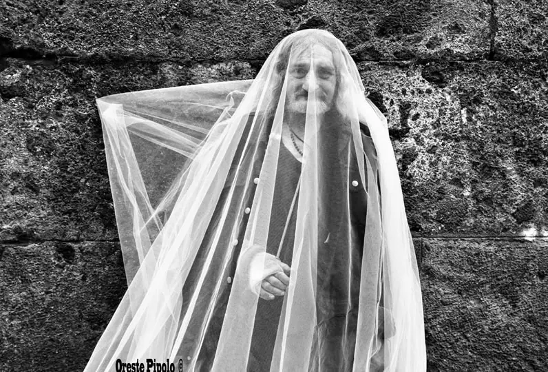 Oreste Pipolo con velo di tulle davanti a muro di pietra.