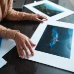 Persona che esamina stampe di fotografie di paesaggi naturali su un tavolo.
