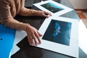 Persona che esamina stampe di fotografie di paesaggi naturali su un tavolo.
