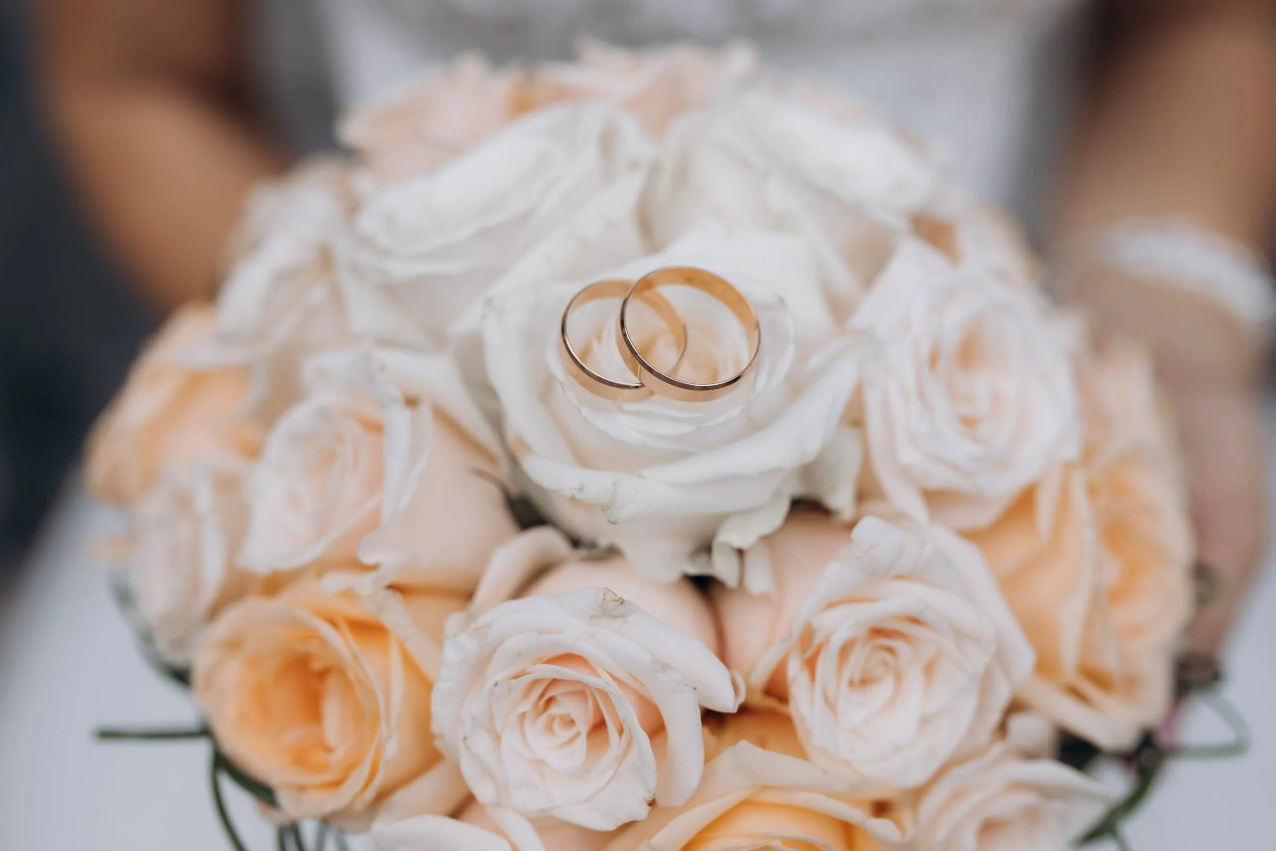 Fedi nuziali posate su un bouquet di rose color pesca e bianco.